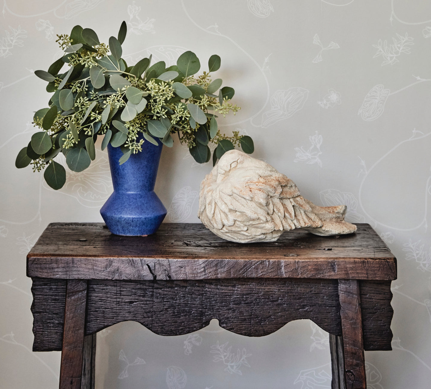 anthurium waltz pale mauve floral wallpaper by august abode, paired with antique English accent table, blue vase & rustic bird sculpture