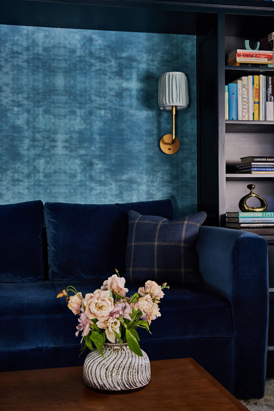 bookmatched wallpaper on grasscloth ground, paired with blue velvet sofa, brass sconce, navy plaid pillow and custom bookshelves.